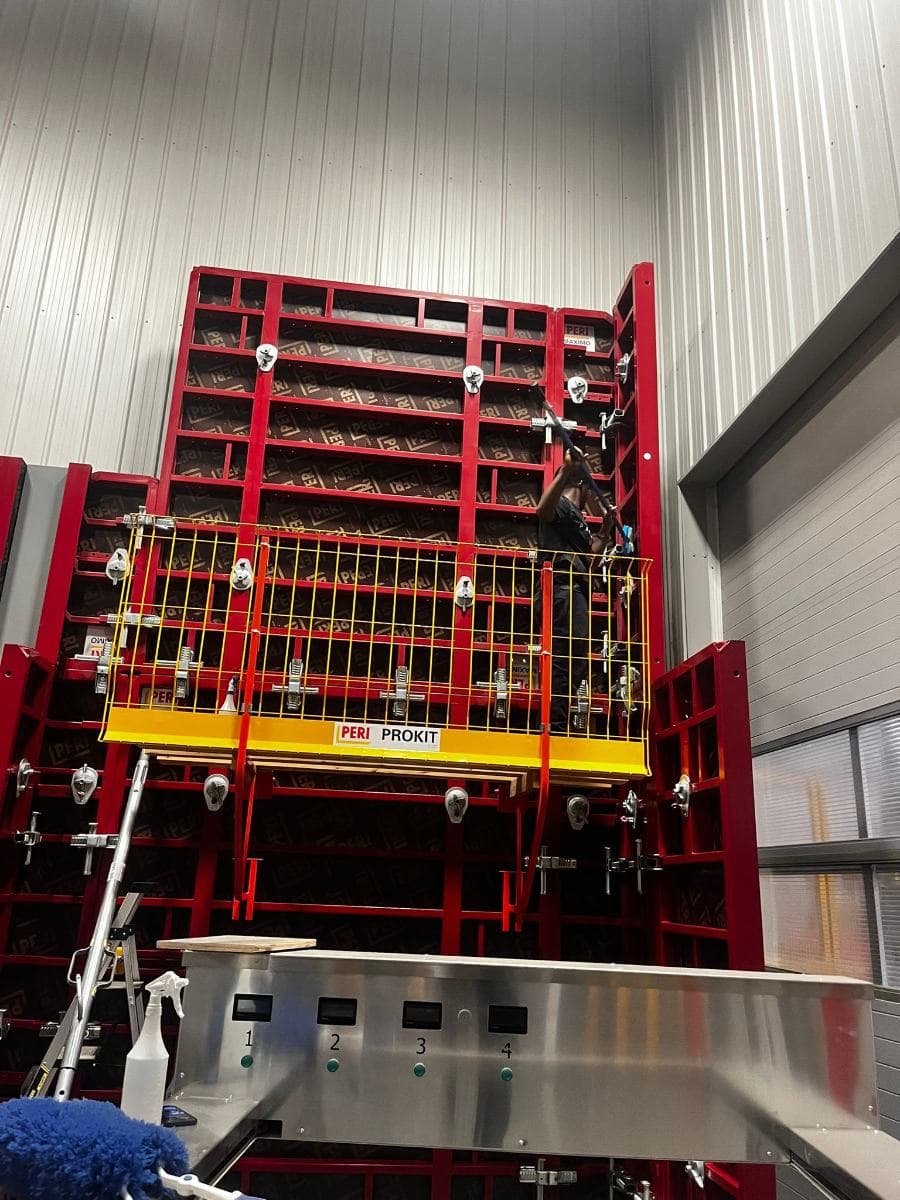 Cleaner on a work platform cleaning tall red formwork panels with an extension pole