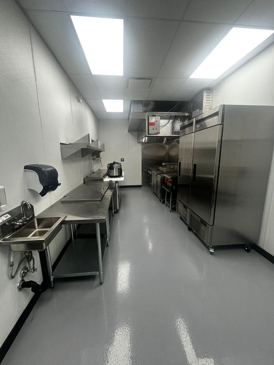 Commercial kitchen with stainless steel prep tables, upright fridges and a clean grey resin floor