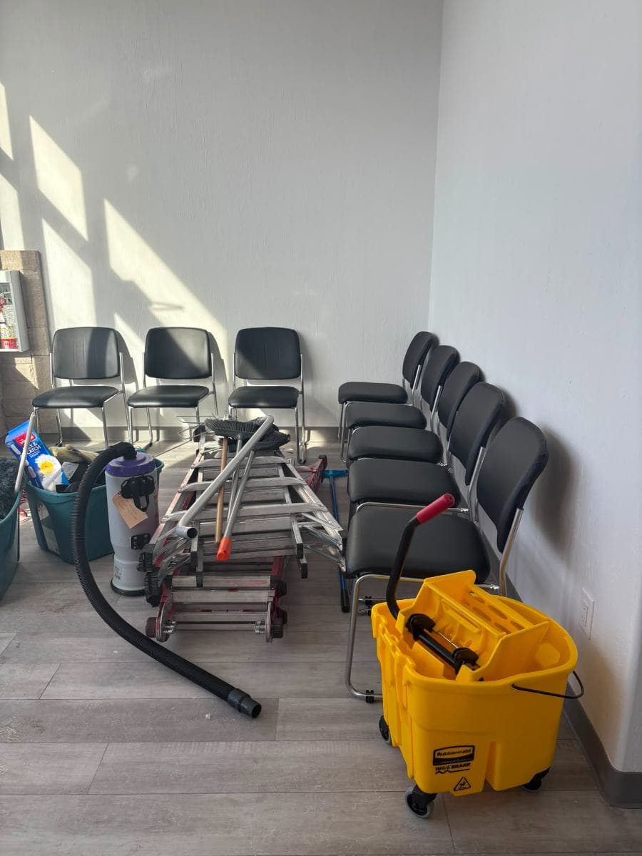 Cleaning equipment set out on site, including a backpack vacuum, mop bucket and ladder