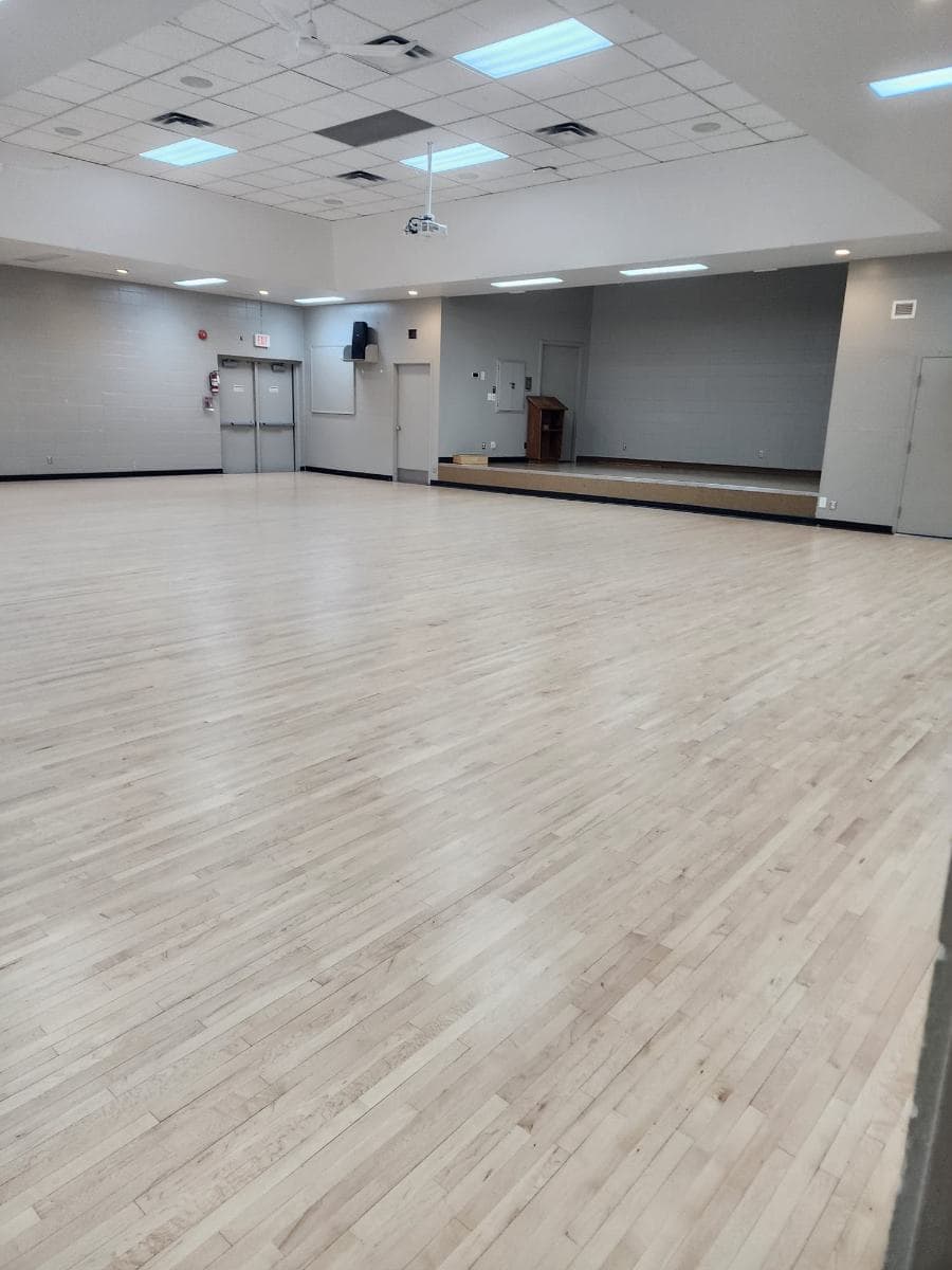 Empty function hall with a freshly cleaned light wood floor and a raised stage